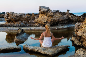 Woman sitting and meditating looking towards the ocean and meditating in lotus pose.  