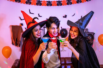 Young happy Asian people dressing Halloween costume, vampire and witch, celebrating in party. Holding and clinking wine glass.