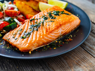 Fried salmon fillet with fried potatoes, lime and vegetable salad served on black plate on wooden table
