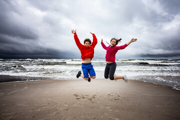 Teenage girl and boy running, jumping on beach
