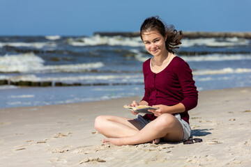 Fototapeta na wymiar Teenage girl reading book sitting on beach