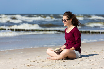 Fototapeta na wymiar Teenage girl reading book sitting on beach