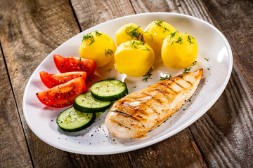 Fried chicken breast with boiled potatoes and fresh vegetables on wooden table
