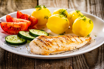 Fried chicken breast with boiled potatoes and fresh vegetables on wooden table
