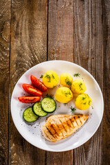 Fried chicken breast with boiled potatoes and fresh vegetables on wooden table
