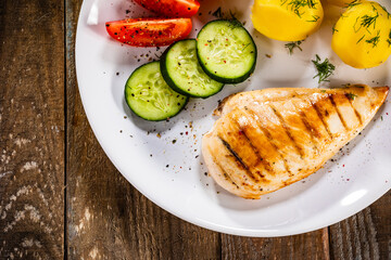 Fried chicken breast with boiled potatoes and fresh vegetables on wooden table
