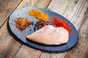 Fresh raw chicken fillet on stone board with spices  on wooden table
