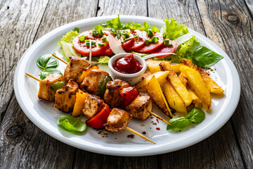 Skewers - grilled meat with French fries and fresh vegetables on wooden background