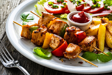 Skewers - grilled meat with French fries and fresh vegetables on wooden background