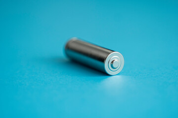 A single rechargeable battery on blue background. Silver alkaline AA battery for different device....