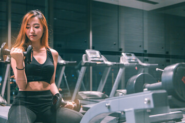 Muscular young asian  woman with beautiful  body doing exercises with dumbbell. Sporty girl lifting weights in gym.