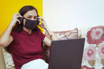 close up of a young indian girl working on her laptop wearing headphones, work from home concept.