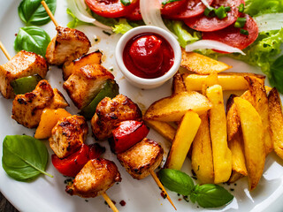 Skewers - grilled meat with French fries and fresh vegetables on wooden background
