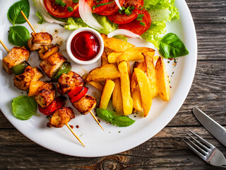 Skewers - grilled meat with French fries and fresh vegetables on wooden background