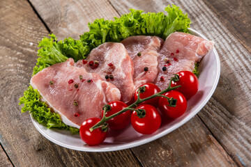 Raw pork chops with fresh lettuce and cherry tomatoes  on plate on wooden background 