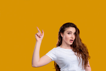 Surprised woman portrait. Aha moment. Shocked lady with open mouth pointing up at copy space isolated on orange wall. Eureka effect. Found solution. Insight idea. Advertising background.