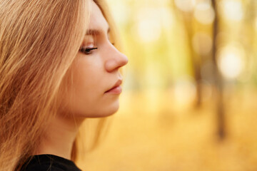 Naklejka premium Closeup autumn portrait of blonde model teen in black t-shirt in public park with sunlight on background. Teen portrait, posing styles, model look book or autumn fall concept