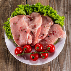 Raw pork chops with fresh lettuce and cherry tomatoes  on plate on wooden background 