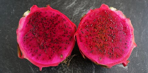 two slice of red dragon fruit, served on a stone pad