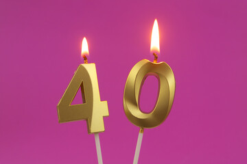 Burning golden birthday candles on pink background, number 40