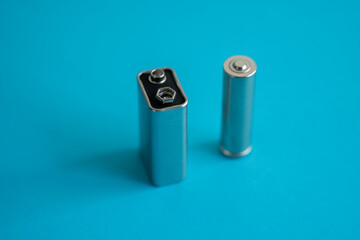 High voltage Volt 9V battery and alkaline AA battery on a blue background. Energy.