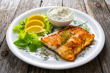 Fish dish - fried cod fillet with cream sauce and lemon served on wooden table
