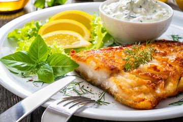 Fish dish - fried cod fillet with cream sauce and lemon served on wooden table
