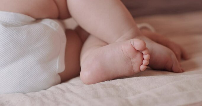 Close up feet of a beautiful sleeping baby, naked, in diapers, on the bed.