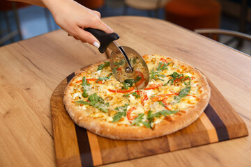 Female hand with circle knife cutting freshly pizza slices