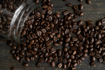 Roasted fresh arabica coffee beans scattered on a table from a little jar on a wooden table. Fresh coffee beans.