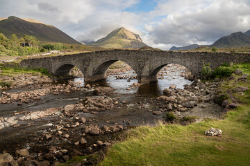 Fototapeta na wymiar Old stone arch bridge at Sligachan, Isle of Skye, Scotland. Cuillin mountains lit by sunset