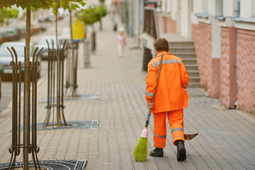 Worker with broom sweeps street from dust and garbage. Street sweeper cleaning road. Municipal...