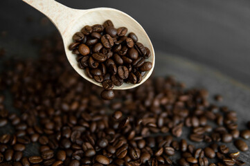 Fresh roasted arabica coffee beans falling from a oaken spoon on a wooden table.