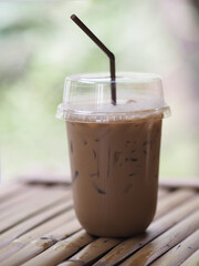 close up view of ice cubes in cold brewed coffee Cappuccino in plastic cup put on bamboo wooden desk blurred background, drink beverage