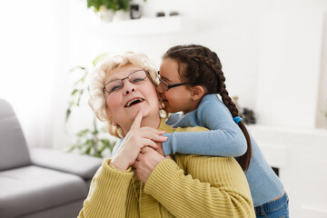 Obraz na płótnie Canvas Senior woman hugging granddaughter while sitting on sofa at home