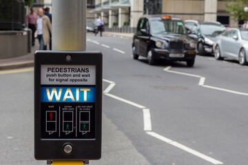 Illuminated 'Wait' pedestrian sign at a pedestrian crossing on a busy road in central London, England