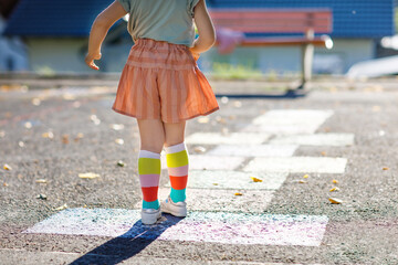 Closeup of leggs of little toddler girl playing hopscotch game drawn with colorful chalks on...
