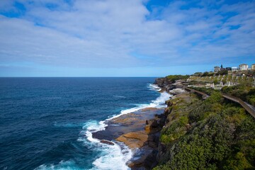 Rock cliffs over the ocean at Bronte Beach with views of the houses at Bondi Beach Sydney NSW Australia