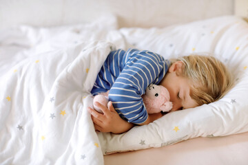 Cute little toddler girl sleeping in bed with favourite soft plush toy lama. Adorable baby child...