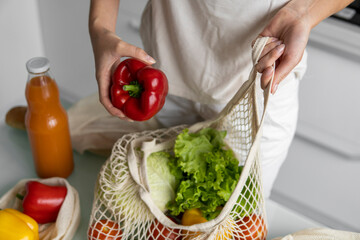 Woman hand holding Reusable eco textile grocery bag with vegetables and takes red and yellow pepper out. Zero waste and plastic free concept. Girl is holding mesh cotton shopper with vegetables.