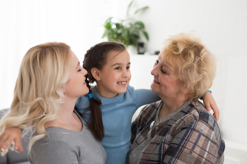 Three generations of women. Beautiful woman and teenage girl are kissing their granny while sitting on couch at home