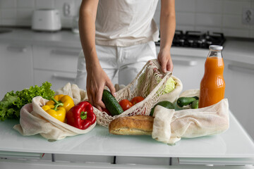 Woman hand holding Reusable eco textile grocery bag with vegetables and takes cucumbers out. Zero waste and plastic free concept. Girl is holding mesh cotton shopper with vegetables.