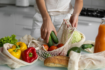 Woman hand holding Reusable eco textile grocery bag with vegetables and takes cucumbers out. Zero waste and plastic free concept. Girl is holding mesh cotton shopper with vegetables.