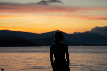 Silhouette of a woman watches sunset over a sea or ocean on a tropical island.