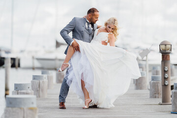 Happy just married couple dancing on the beach with yachts in the background. Wedding by the sea on the beach