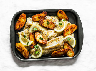 Baked fish fillet and potatoes on a baking sheet on a light background, top view. Mediterranean style lunch