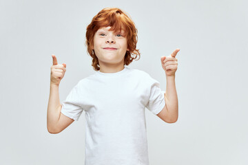 Cheerful red-haired boy gesturing with his hands index fingers smile white t-shirt Copy Space gray...