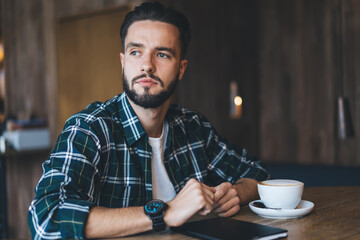 Serious man looking away while drinking coffee in cafe