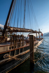 Detail of an ancient sailing ship in the port of Malcesine towards the sunset on Garda Lake with the reflections of the sun that stand out on the wood of the boat in a late summer day. Verona, Veneto,