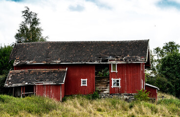 Decaying and abandoned old red barn with holes in the walls and roof.